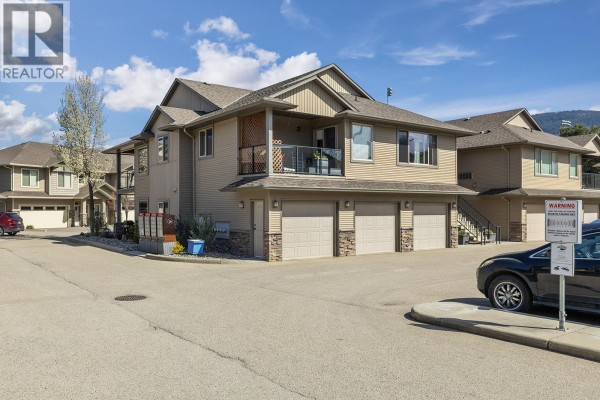 Corner view of a townhouse complex with garage doors, balconies, and surrounding pavement. - 3350 Woodsdale Road Unit# 401, Lake Country