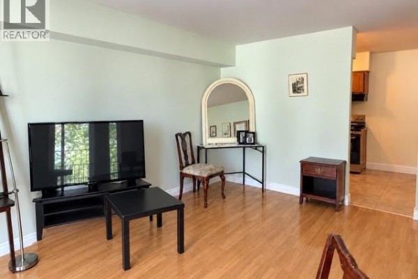Living area with light wood floors, a microwave, chairs, and a large window. - 3355 Sandwich Street Unit# 304, Windsor