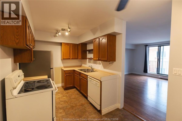 View of a small kitchen with wood cabinets, white stove, and stainless steel refrigerator. - 3355 Sandwich Unit# 310, Windsor