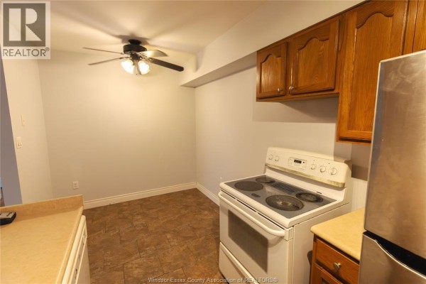 Kitchen area with white stove, wood cabinets, stainless steel refrigerator, and ceiling fan. - 3355 Sandwich Unit# 310, Windsor