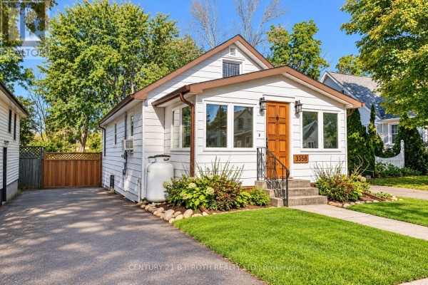 Side view of white house exterior with propane tank, wooden fence, and driveway. - 3358 Muskoka Street, Severn