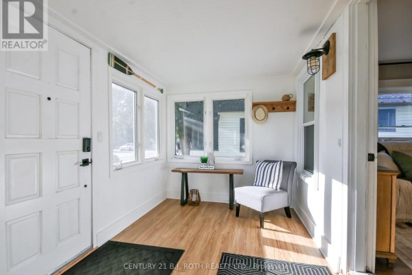 Bright sunroom with white walls, large windows, wood floors, and nautical decor. - 3358 Muskoka Street, Severn