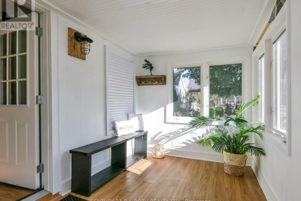 Sunroom with white walls, wood floors, a bench, plant, and windows overlooking the street. - 3358 Muskoka Street, Severn