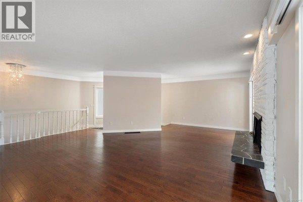 Living room interior showing dark hardwood floors, white brick fireplace, and neutral-colored walls. - 336 Stannard Ave, Victoria