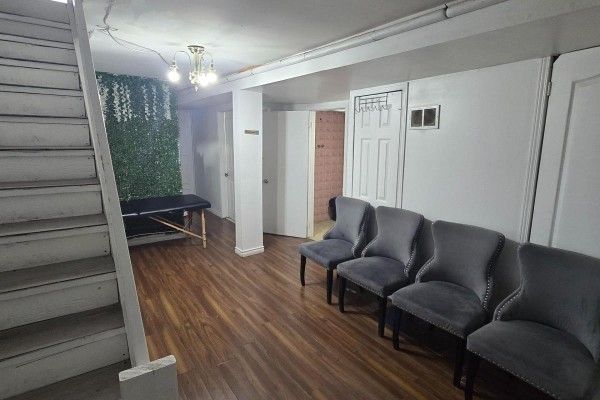 Waiting area with grey upholstered chairs and a massage table next to a staircase. - 336 Weston Road, Toronto