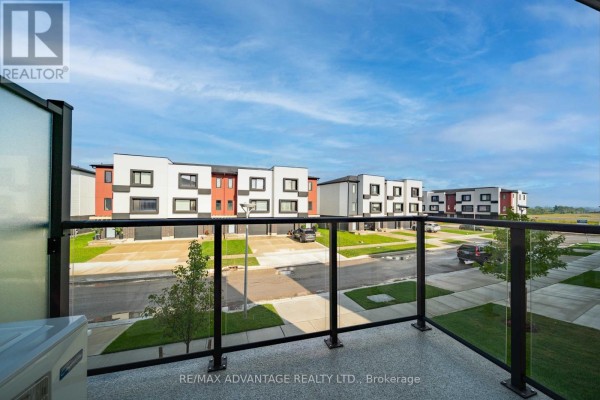 Balcony view showing townhouses, street, and green landscaping under a blue sky. - 3363 David Milne Way, London South