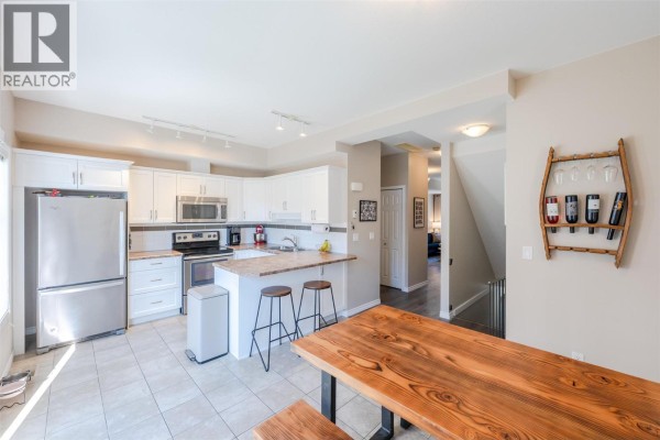 Kitchen and dining area with white cabinets, stainless steel appliances, and a wooden table. - 3363 Wilson Street Unit# 125, Penticton