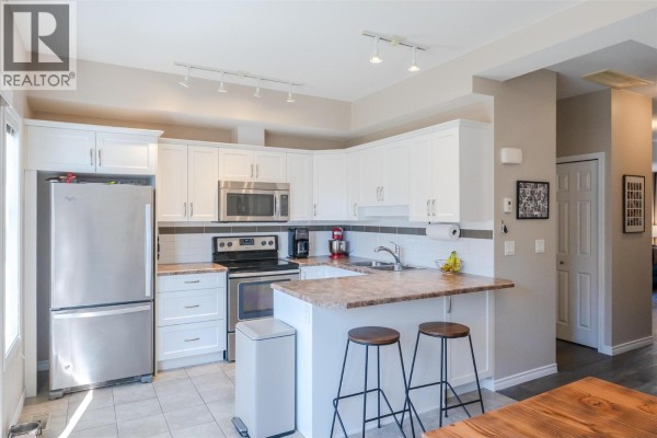 Corner view of the kitchen featuring white cabinetry, stainless steel appliances, and a breakfast bar. - 3363 Wilson Street Unit# 125, Penticton