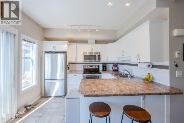 Kitchen with white cabinets, stainless steel appliances, tiled floor, and a large window. - 3363 Wilson Street Unit# 125, Penticton