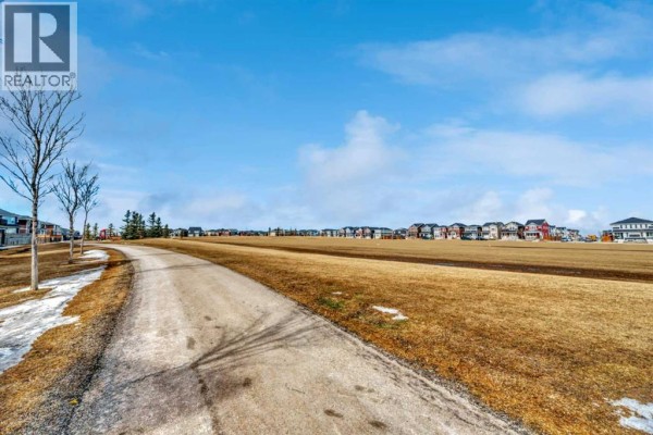 Grassy field with a walking path and distant houses under a bright blue sky. - 337, 301 Redstone Boulevard Ne, Calgary
