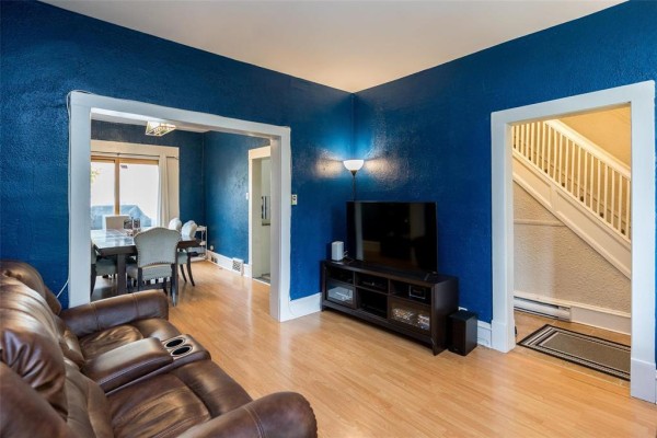 Living room with blue textured walls, leather sofa, television, and doorway to dining area. - 337 Bannerman Avenue, Winnipeg