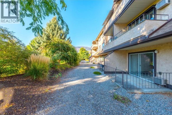 View of building exterior with gravel walkway, trees, and distant hills. - 337 Mckinney Road Unit# 107, Oliver