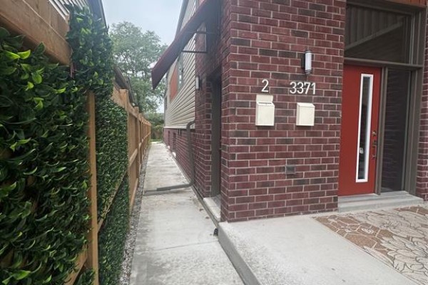 Side pathway between brick duplex exterior and a green artificial hedge fence. - 3371 Byng Unit# 2, Windsor