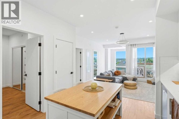 View of living room from kitchen, with large windows and city view. - 338, 110 18a Street Nw, Calgary