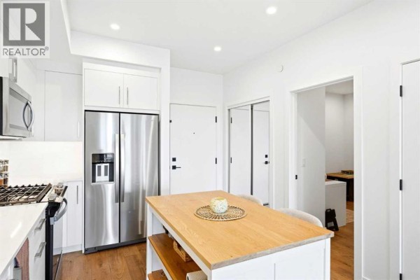 White kitchen with stainless steel appliances, island, and entrance to other rooms. - 338, 110 18a Street Nw, Calgary