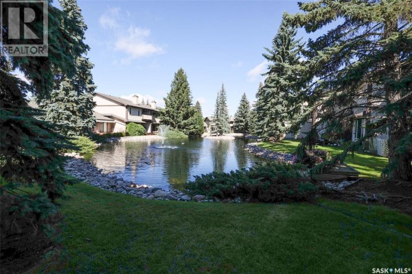 View of the man-made pond with a fountain and surrounding trees. - 338 Avon Drive, Regina