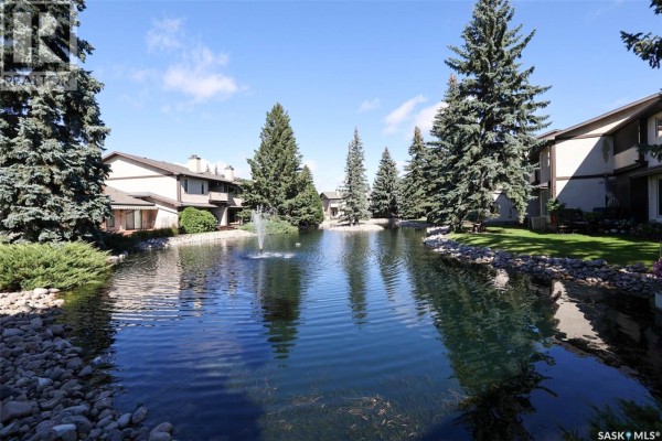 Man-made pond with a fountain and trees reflecting in the blue sky. - 338 Avon Drive, Regina