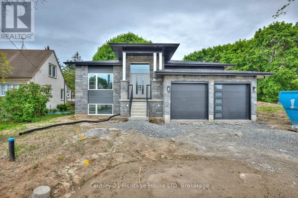 Modern house exterior with grey stone and metal siding, two dark grey garage doors, and gravel landscaping. - 338 Sugarloaf Street, Port Colborne