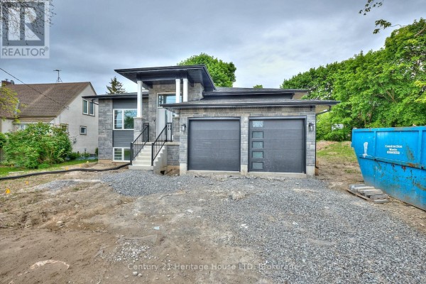 Close-up of modern house exterior featuring grey stone siding, two garage doors, and visible construction debris. - 338 Sugarloaf Street, Port Colborne
