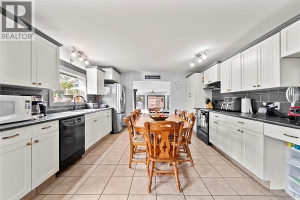 Long white kitchen with wood cabinets, tiled floor, and dining table. - 3381 Trinity Valley Road, Enderby