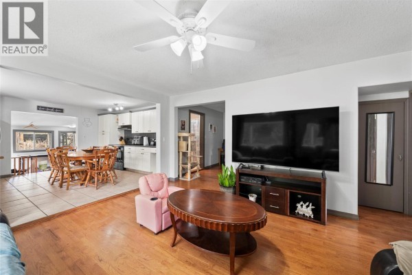 Living room with wood floor, large TV, pink armchair, and view of dining area. - 3381 Trinity Valley Road, Enderby