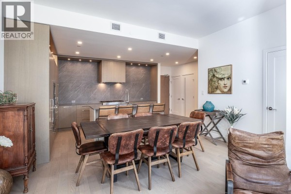 Dining area with a large table and chairs adjacent to a contemporary kitchen. - 3389 Lakeshore Road Unit# 413, Kelowna
