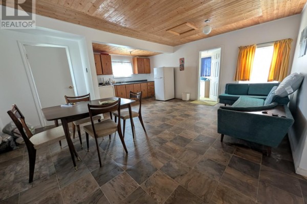 Open concept living area with a kitchen, dining table, and teal sofa with wood-paneled ceiling. - 339 Main Road, Fogo Island
