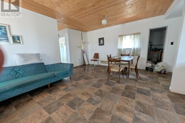 Living and dining area with teal sofa, wooden dining table, and checkered tile flooring. - 339 Main Road, Fogo Island