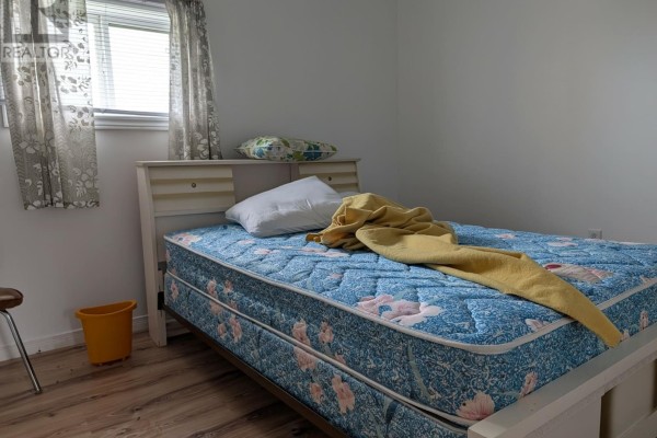 Bedroom with a queen-size mattress on a white bed frame, a window with patterned curtains. - 339 Main Road, Fogo Island