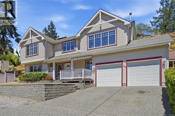Front view of a large, two-story residential home with beige siding and dark red trim, set against a sloping hillside. - 339 Nottingham Dr, Nanaimo
