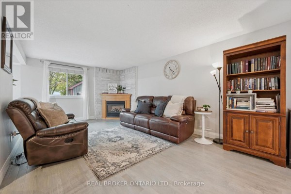 A cozy living room with a leather sofa, armchair, fireplace, and bookshelf. - 339 Strathallan Street, Centre Wellington