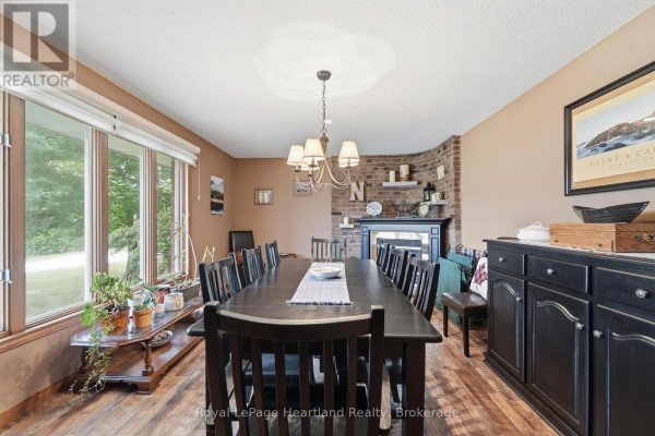 Dining room with a large dark wood table, brick fireplace, and windows overlooking trees. - 33950 Bachand Street, Bluewater