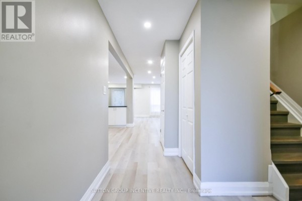 A hallway with light wood flooring, grey walls, and a view into a bright living area. - 33b Cundles Road E, Barrie
