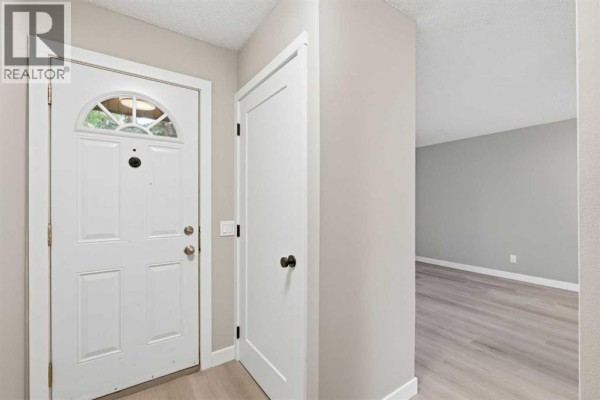 Interior foyer with a white front door, closet, and view into a room with wood-look flooring. - 34, 420 Grier Avenue Ne, Calgary