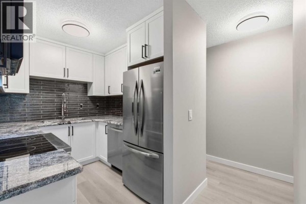 Compact kitchen with white cabinetry, stainless steel appliances, grey tile backsplash, and granite countertops. - 34, 420 Grier Avenue Ne, Calgary
