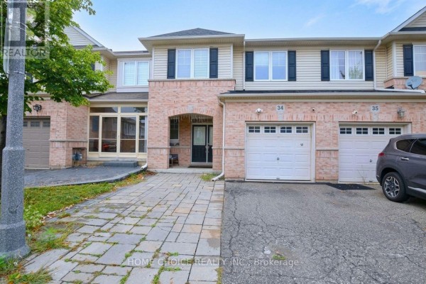 Street view of the townhouse exterior, number 34, with a paved driveway and garage doors. - 34 - 3275 Stalybridge Drive, Oakville