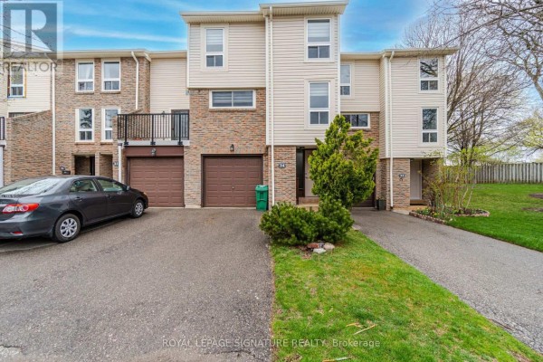 View of a townhouse exterior with a driveway, garage, and green lawn. - 34 - 7251 Copenhagen Road, Mississauga