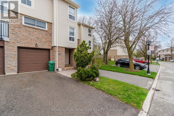 Close-up of a townhouse entrance with a paved walkway, garage, and shrubs. - 34 - 7251 Copenhagen Road, Mississauga