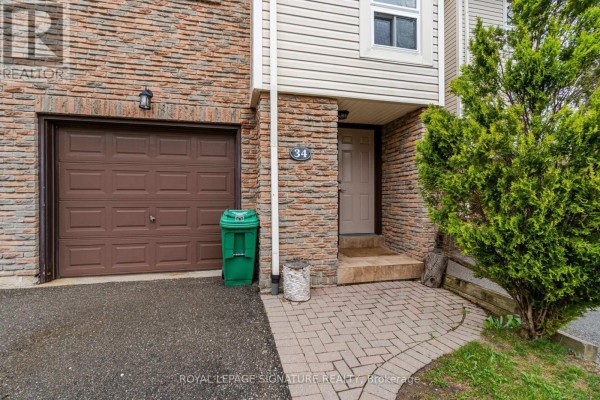 Townhouse unit 34 exterior detail showing the garage door, entrance, and brickwork. - 34 - 7251 Copenhagen Road, Mississauga