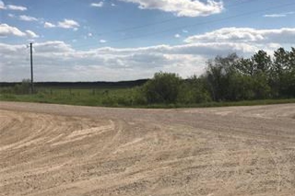 A dirt road intersection with a grassy field and trees in the background. - 34 4-8e Road Nw, La Broquerie