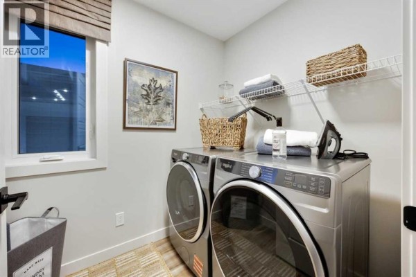 Two-story detached house with dark siding, brick garage, and gabled roof. - 34 Amblefield Common Nw, Calgary