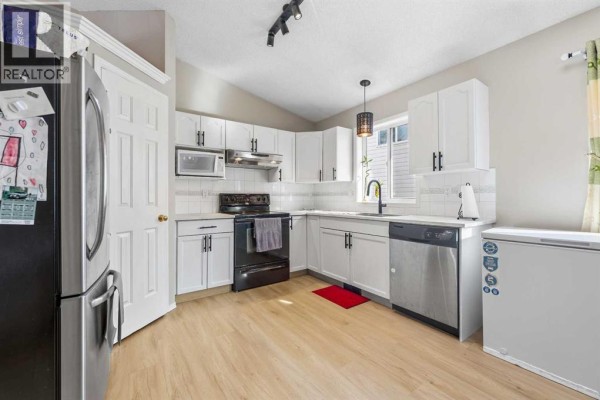 White kitchen with black appliances, subway tile backsplash, and stainless steel refrigerator. - 34 Applestone Park Se, Calgary