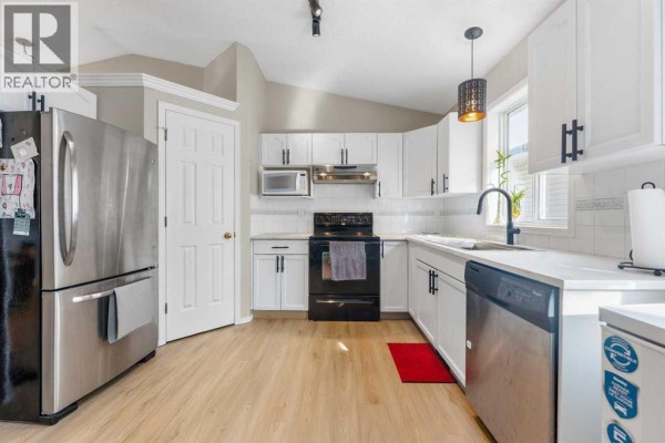 White kitchen with white cabinets, black hardware, stainless steel dishwasher, and white countertops. - 34 Applestone Park Se, Calgary