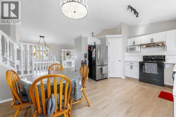 Open concept living space with dining table, staircase, and kitchen with stainless steel refrigerator. - 34 Applestone Park Se, Calgary