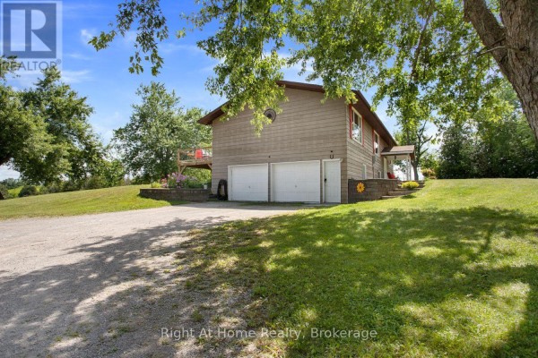 Side view of a two-story house with wood siding and a three-car garage on a hill. - 34 Birch Point Road, Kawartha Lakes