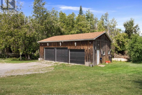 Detached wooden garage with three black overhead doors and a gravel driveway in a grassy area. - 34 Birch Point Road, Kawartha Lakes