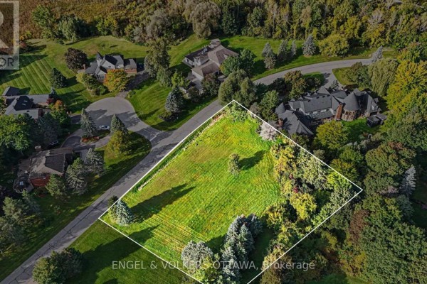 Overhead view of a green, irregular-shaped lot outlined in white, adjacent to a paved road and wooded area. - 34 Cedarhill Drive, Ottawa