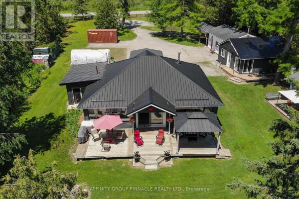 Aerial view of a dark grey bungalow with a black metal roof and a large wooden deck. - 34 Coldstream Road, Kawartha Lakes