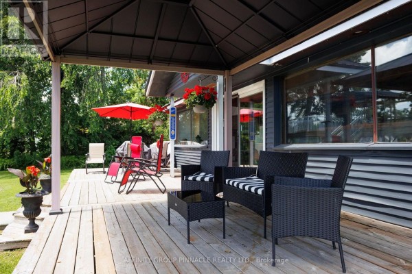 Covered porch area with wicker furniture and a coffee table overlooking a wooden deck and yard. - 34 Coldstream Road, Kawartha Lakes