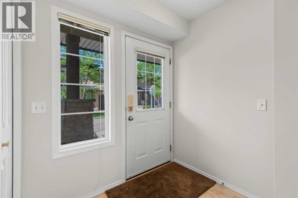 Interior view of a townhouse entrance with a white door, windows, and light grey walls. - 34 Eversyde Common Sw, Calgary